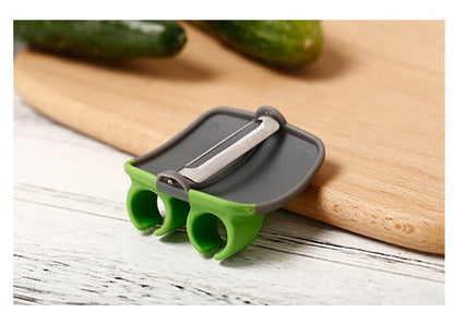 Green and grey two-finger palm peeler on a wooden cutting board, stainless steel blade on top